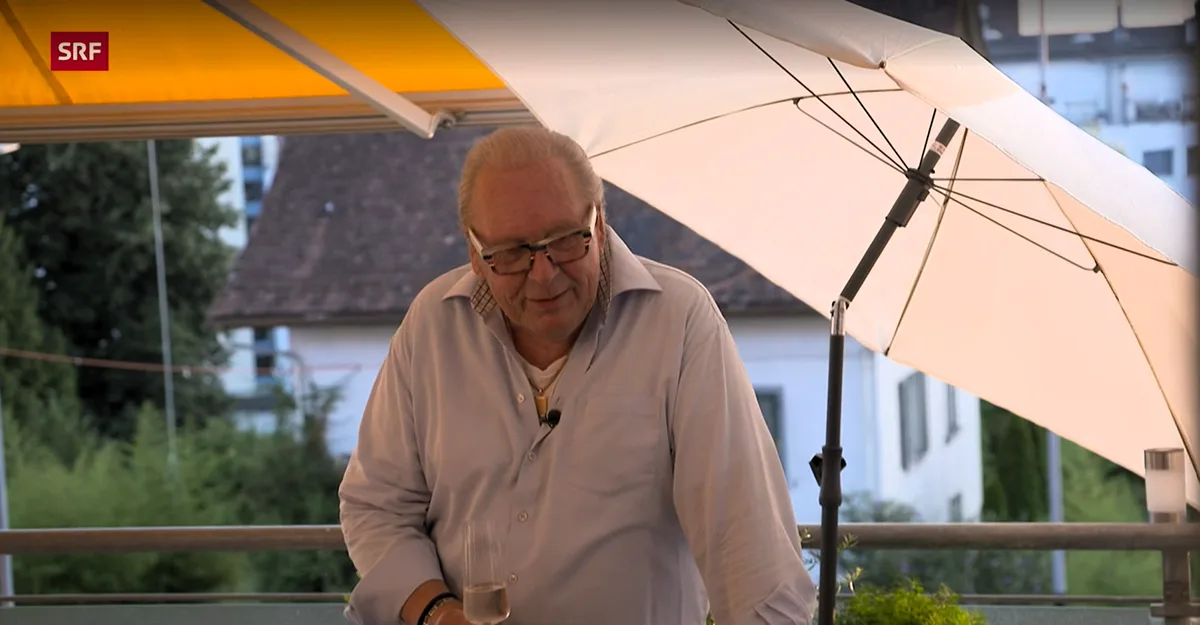 Man sieht einen Mann auf einem Balkon mit Sonnenschirm.